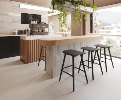 Cocina moderna tipo café con barra de madera clara, sillas negras y plantas colgantes, diseño contemporáneo luminoso.